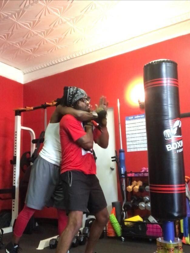 Two people practicing self-defense techniques in a gym with red walls and various fitness equipment.